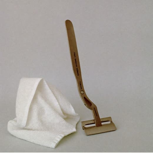 An open straight razor beside a folded white towel on a plain pastel surface